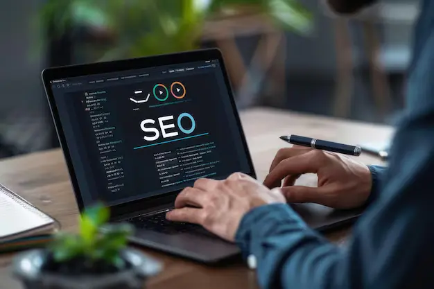 مكتب عمل عليه حاسوب محمول بشاشة داكنة تعرض كلمة SEO وقلم موضوع بجانب لوحة المفاتيح